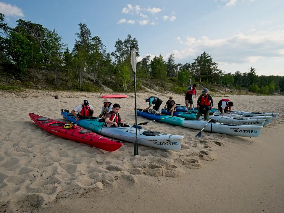 The group gathers with brightly colored kayaks on the sand before turning toward Pictured Rocks.