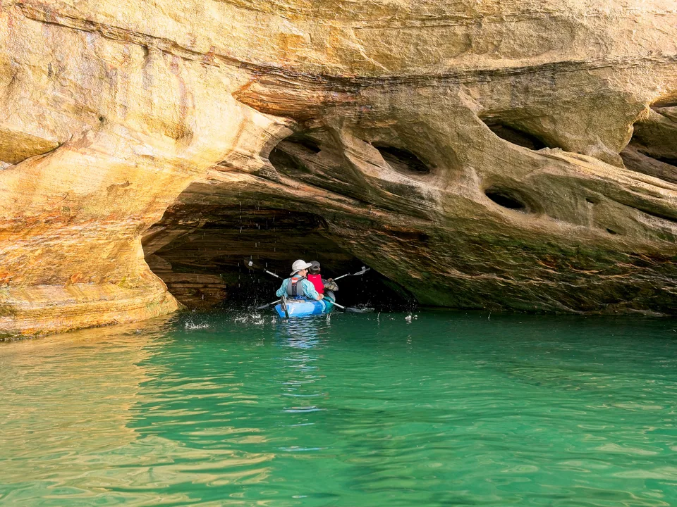 A kayak slips beneath a glowing sandstone overhang and into emerald water.